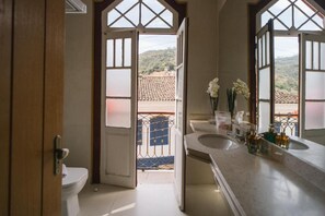 Een badkamer met toilet, wastafel en een groot raam met uitzicht op een betegeld dak en heuvels.