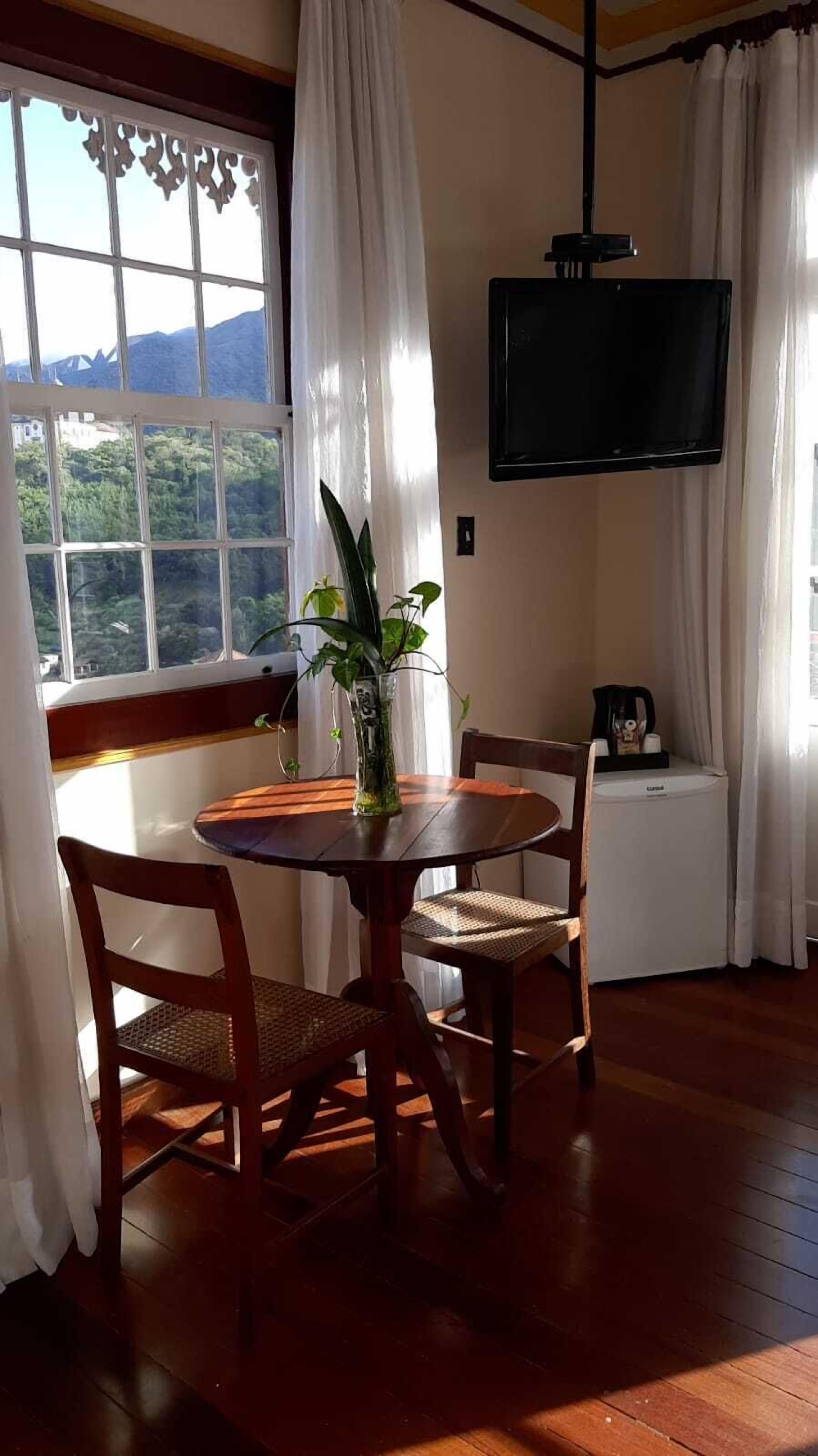 A room with a wooden table and chairs, a potted plant, a television, and a view of mountains through a window.
