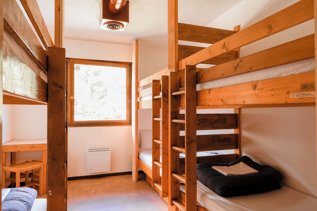 Une chambre avec un lit superposé, une fenêtre, un radiateur et un bureau en bois.