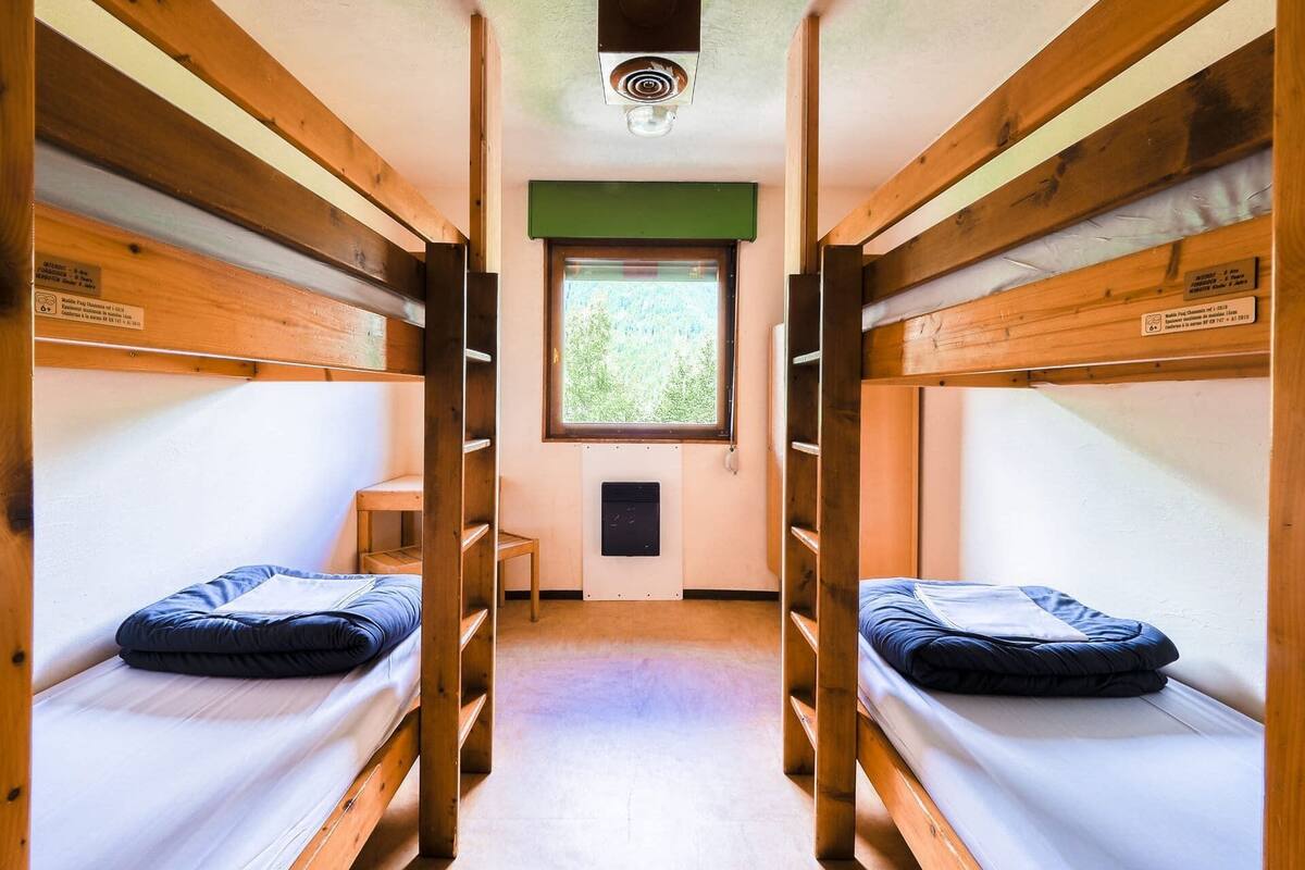 Una habitación pequeña con dos literas, una ventana que da a zonas verdes y un estante con una lámpara.