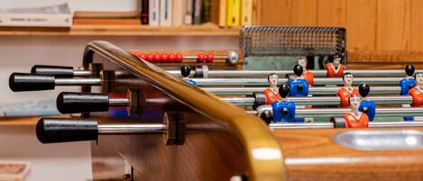 A foosball table with a wooden base and metal rods, set against a backdrop of bookshelves.