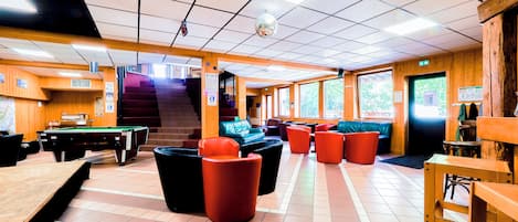 A billiards room with a pool table, multiple seating areas, and a staircase leading to upper levels.
