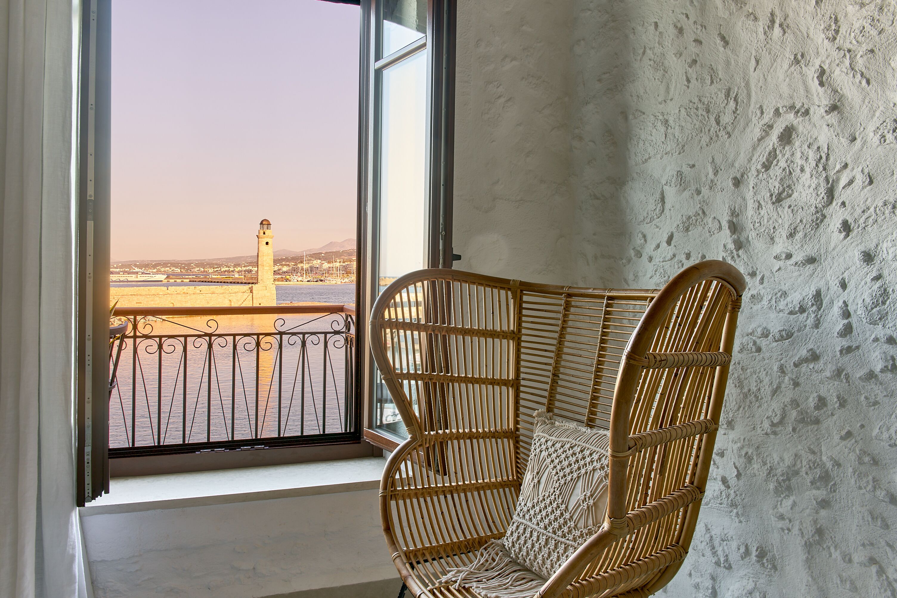 Una silla de mimbre junto a una ventana con vistas a un faro y un puente.