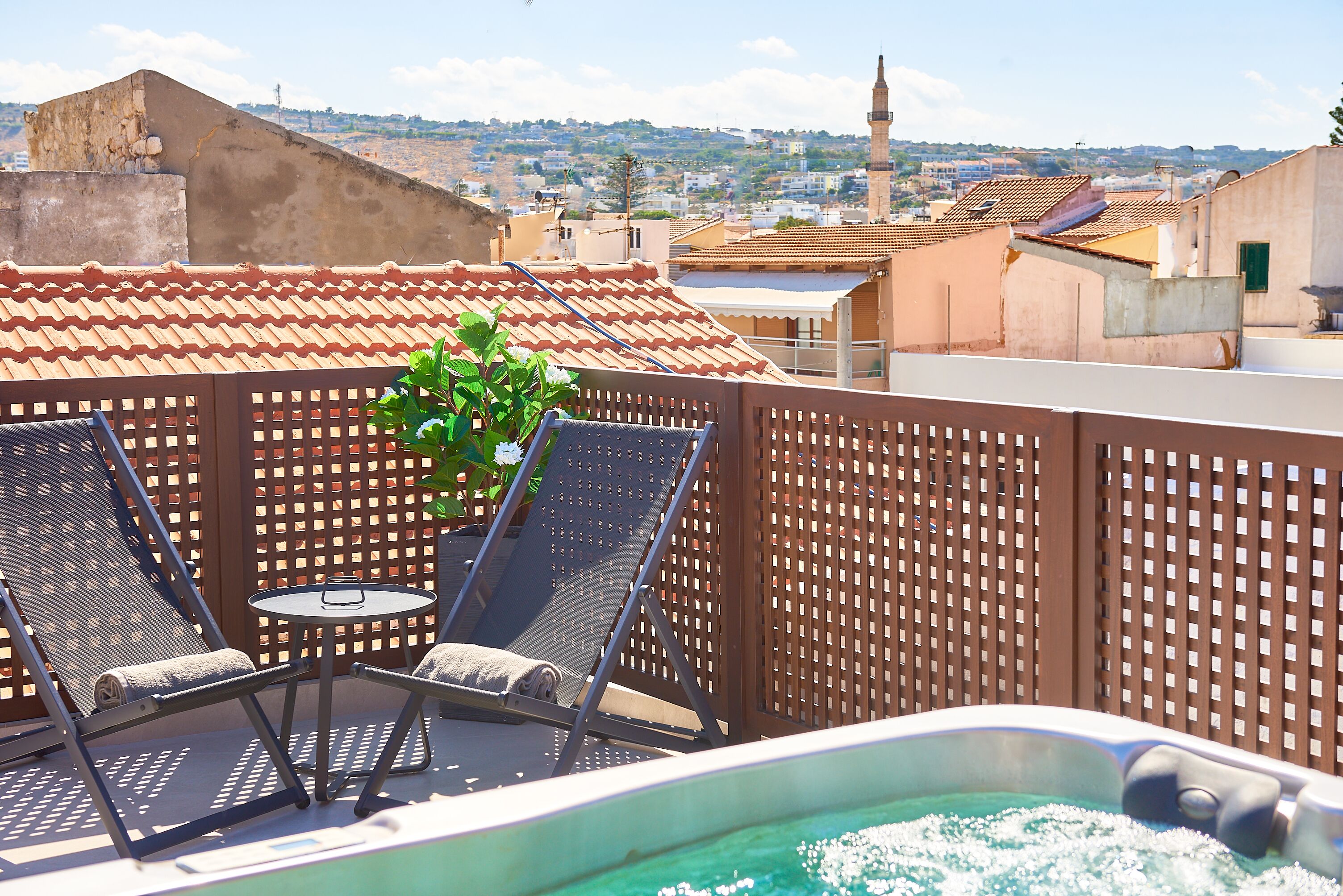 A rooftop terrace with two lounge chairs, a small table, and a hot tub.