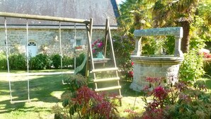 Un edificio de piedra con techo de paja, un columpio y una fuente en un jardín.