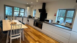 A modern kitchen with wooden flooring, a dining table, and a built-in oven. - Relaxing Luxury Holiday Home (Llangollen)