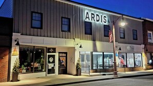 En bygning med et skilt 'ARDIS' på facaden, butikker med synlige skilte og et flagstang med det amerikanske flag.