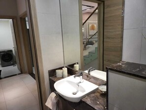 A modern bathroom with a large mirror, two sinks, and a visible laundry machine in the background. - Mirdif Hills Apartaments (Dubai)