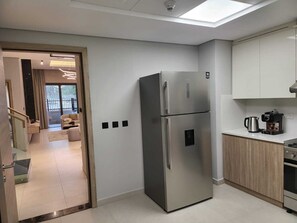 A modern kitchen with a stainless steel refrigerator, wooden cabinets, and a coffee maker on the countertop. - Mirdif Hills Apartaments (Dubai)