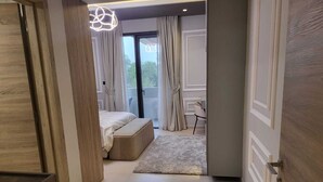 A modern bedroom with a bed, a desk, and a view through a glass door. - Mirdif Hills Apartaments (Dubai)
