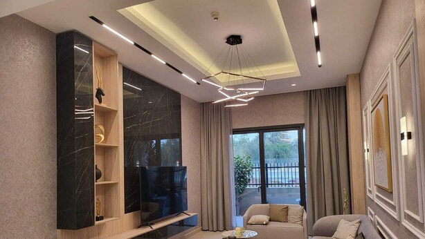 A modern living room with a flat-screen TV, a sofa, and a coffee table. - Mirdif Hills Apartaments (Dubai)