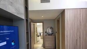 A modern hotel room with a television displaying a menu, a wooden wardrobe, and a hallway leading to a bathroom. - Mirdif Hills Apartaments (Dubai)
