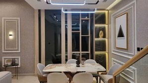 A modern dining area with a marble table, cushioned chairs, and a staircase. - Mirdif Hills Apartaments (Dubai)