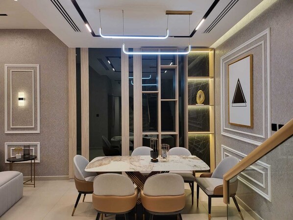 A modern dining area with a marble table, cushioned chairs, and a staircase.