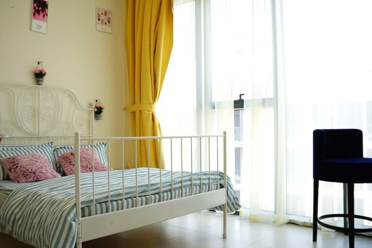 Une chambre à coucher avec un lit en métal blanc, une literie à rayures et un rideau jaune.