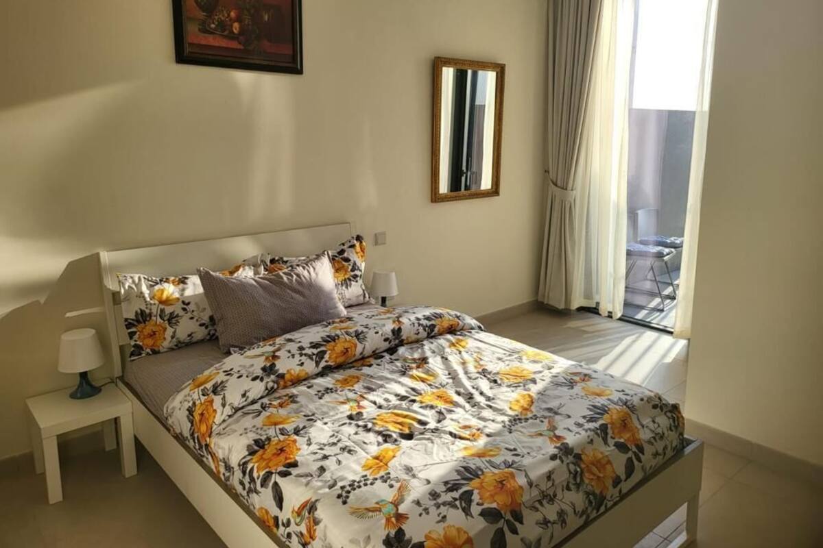 Une chambre à coucher avec un lit, des tables de chevet, un miroir et une fenêtre avec des rideaux.