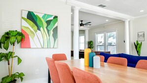 Un coin repas avec une table en bois et des chaises orange, une peinture abstraite aux couleurs vives et une plante en pot.