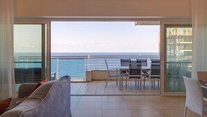 En balkon med havudsigt og et fjernt skib, møbleret med et bord og stole.