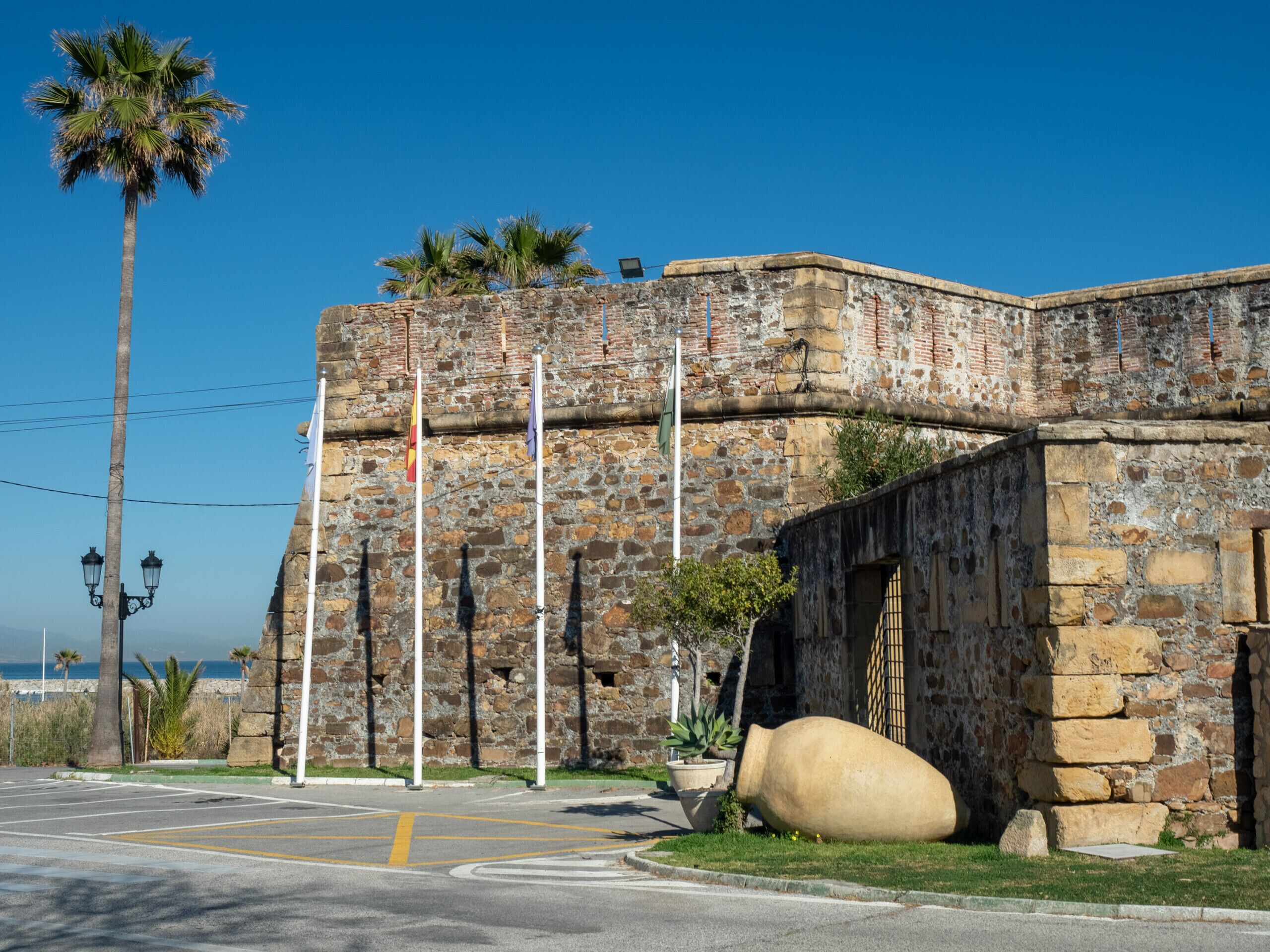 A stone building with a palm tree, a large pot, and a flagpole.
