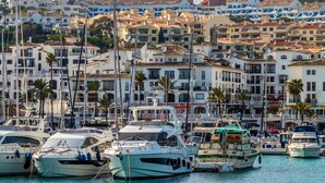 A marina with multiple yachts docked, surrounded by multi-story buildings with balconies and a hilly backdrop. - Coto Real 2408 Kiznos Sun & Relax (Manilva)
