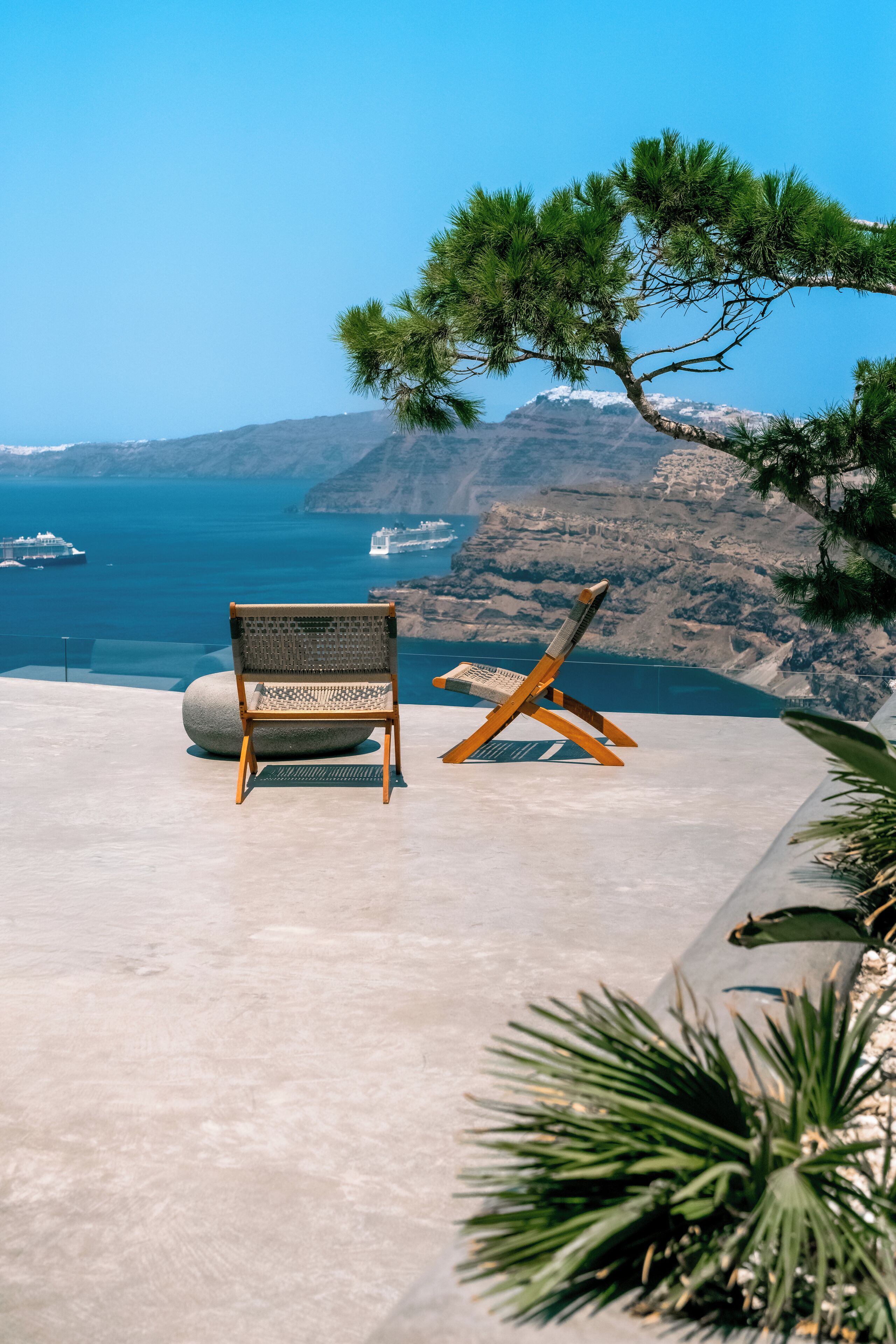 A bench and a lounge chair on a terrace overlooking a coastal landscape with a ship in the distance.