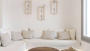 A modern living room with a white sofa, two wooden side tables, and a pendant light. - Nelya Suites (Santorini)