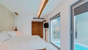 A modern bedroom with a bed, a TV, and a large window overlooking a pool. - Nelya Suites (Santorini)