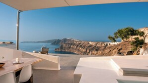 A modern outdoor dining area with a view of the sea and cliffs. - Nelya Suites (Santorini)