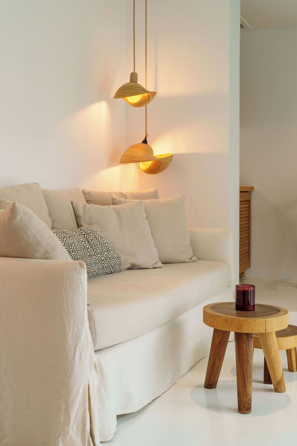 A modern living room with a white sofa, patterned cushions, and a wooden coffee table. - Nelya Suites (Santorini)