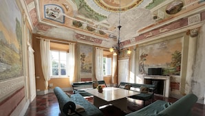 Una habitación amplia con una mesa grande y cuatro sillas tapizadas en verde, una chimenea y un televisor.