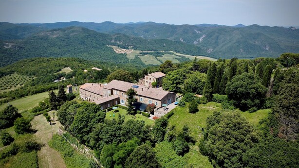 Un edificio de piedra grande con varias habitaciones, rodeado de abundante vegetación y colinas al fondo.
