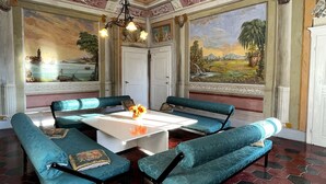 Una habitación con una mesa blanca, sillas tapizadas en color aguamarina, una araña y grandes cuadros de paisajes en las paredes.