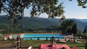 Una mesa con mantel rojo y sillas, con vistas a una piscina y montañas.
