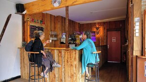 Un espace bar avec des murs en bois, un comptoir et des tabourets. On peut y voir des bouteilles et des verres sur le comptoir, ainsi qu’un menu écrit à la craie.