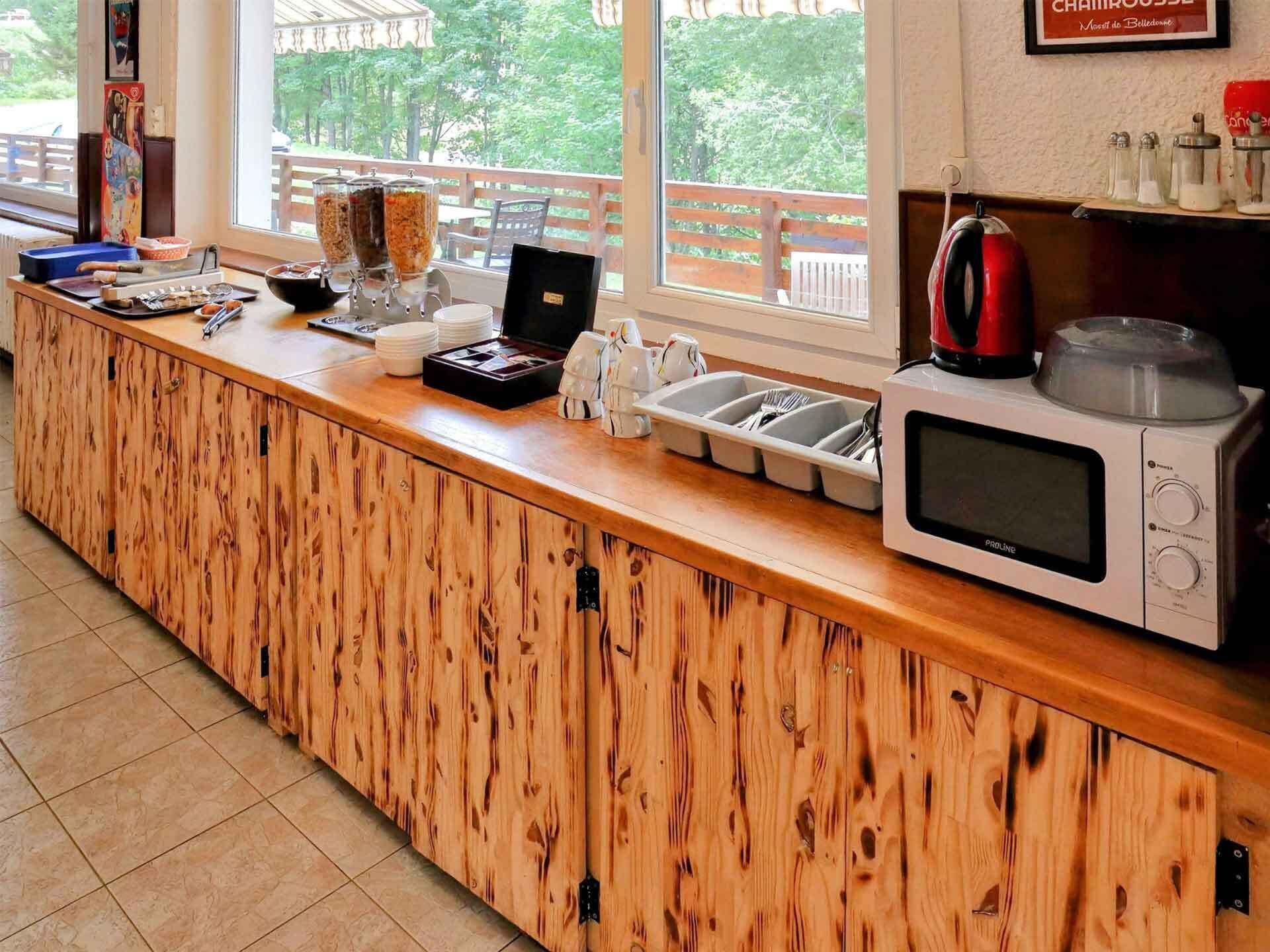 Una encimera de madera con microondas, saleros y pimenteros, hervidor y cafetera.