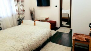 A bedroom with a large bed, a TV mounted on the wall, a small table, and a chair. - The Sharkov House (Satovcha)