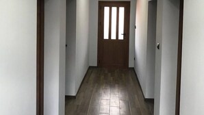 A hallway with a wooden door at the end, white walls, and a tiled floor. - The Sharkov House (Satovcha)