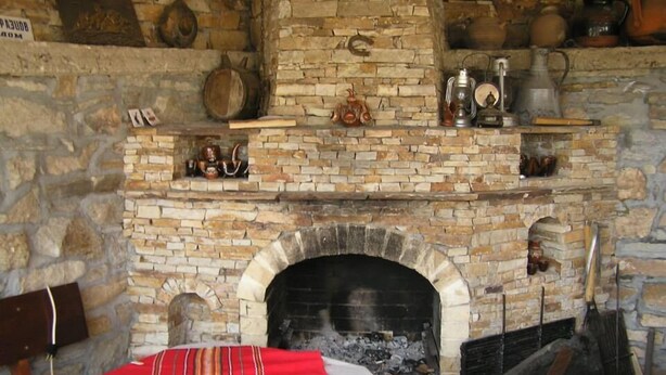 A stone fireplace with a table in front, surrounded by rustic decor. - The Sharkov House (Satovcha)