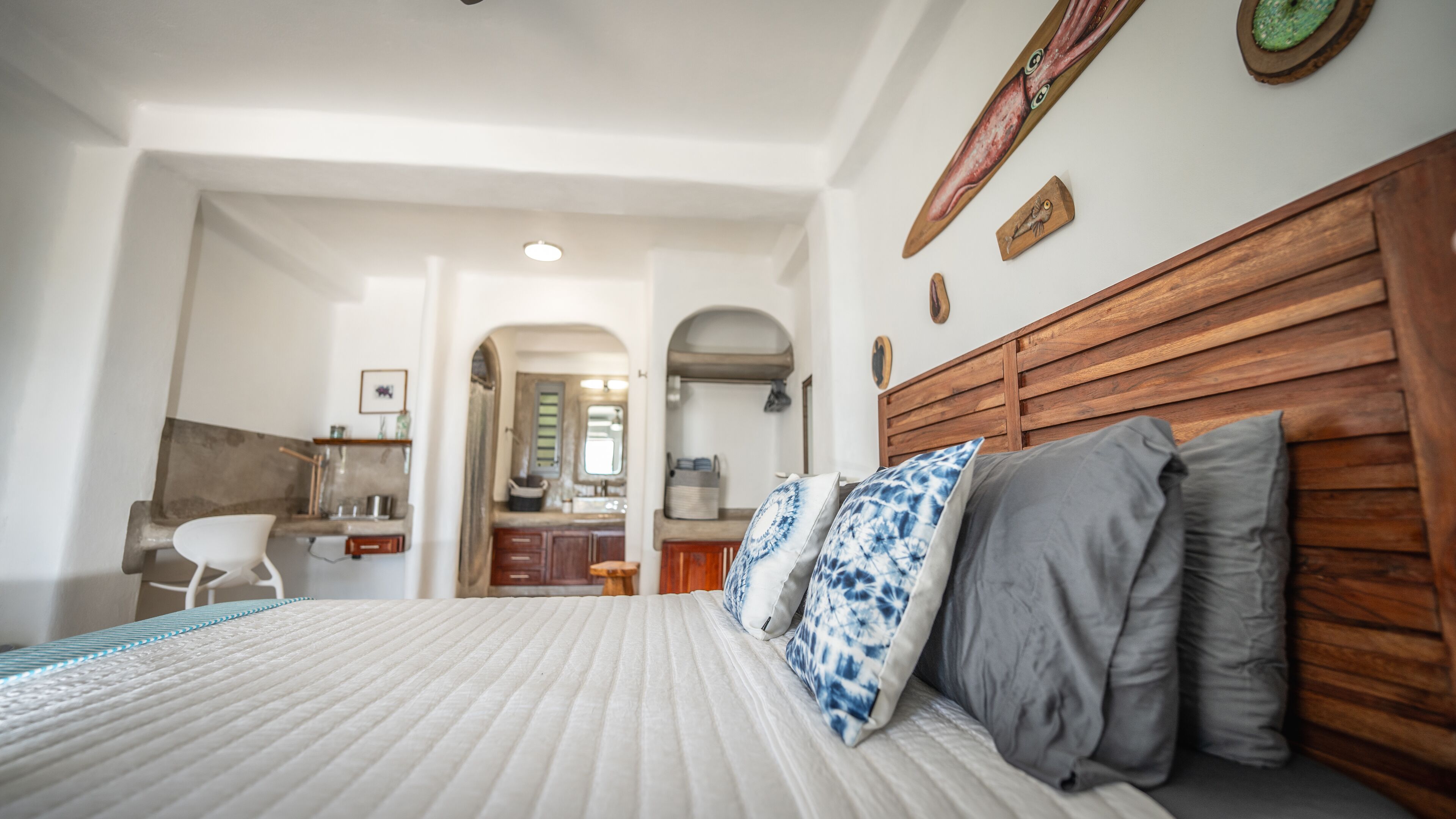 A bedroom with a bed, wooden headboard, and a kitchenette in the background.