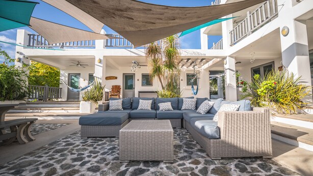A spacious outdoor seating area with a large sofa and wicker chairs, surrounded by potted plants and a stone floor. - La Casona Blanca Location Location  (Esperanza)