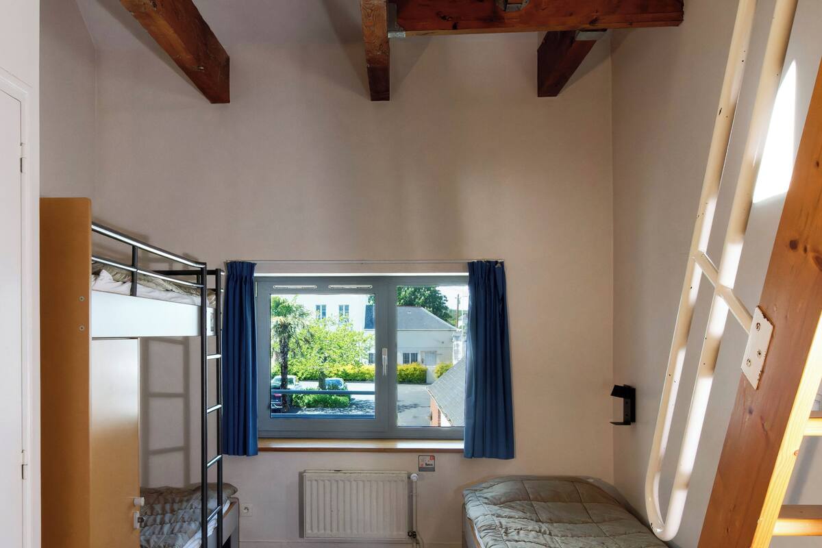 A dormitory room with bunk beds, a window with curtains, and a radiator.