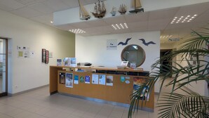 A reception desk with a wooden counter, a round mirror, and various informational posters. - Auberge de Jeunesse HI Cherbourg (Cherbourg-en-Cotentin)