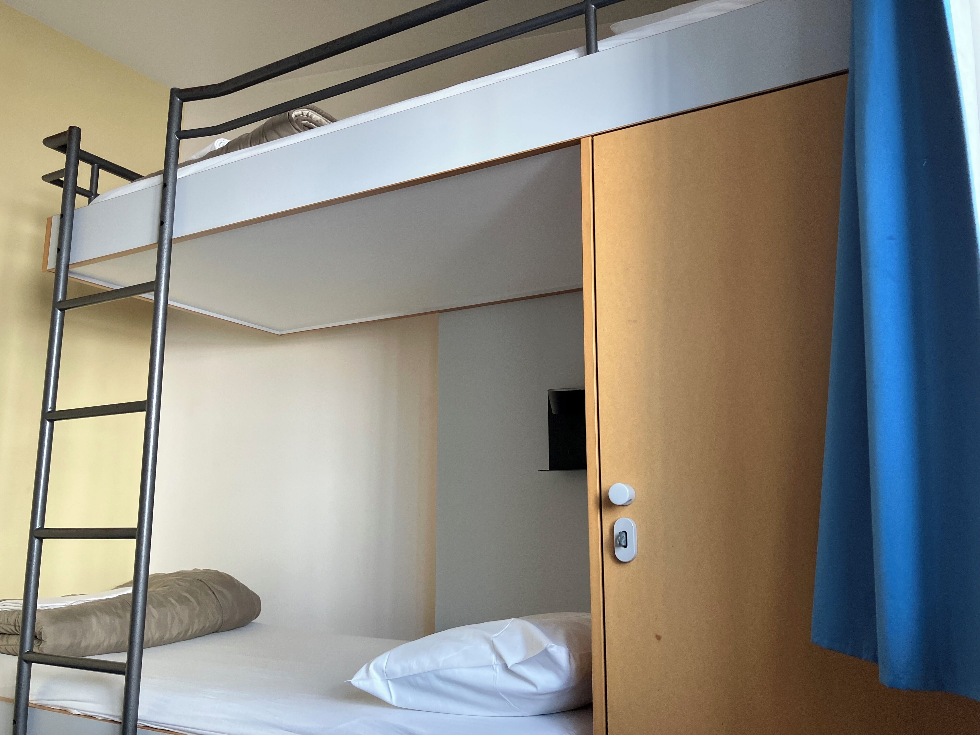 Un llit superposat amb una escala, un armari de fusta i un petit televisor.