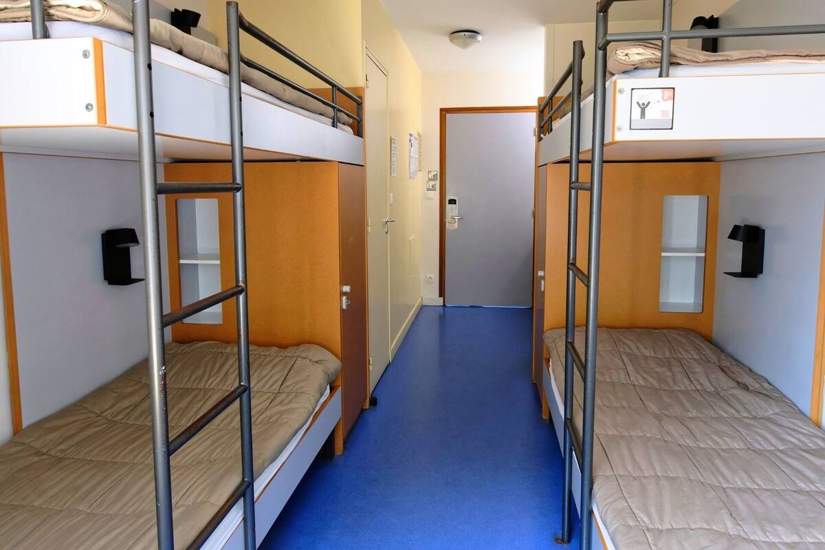 A dormitory room with bunk beds, a blue carpet, and a door with a sign.