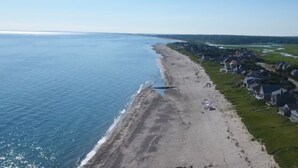 An aerial view of a coastal residential area with houses along the beach and a road leading through the community.