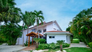 A two-story house with a covered patio, surrounded by lush greenery and palm trees. - casa de campo villa 204 (La Romana)