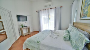 A bedroom with a bed, a TV, a desk, and a window with curtains. - casa de campo villa 204 (La Romana)
