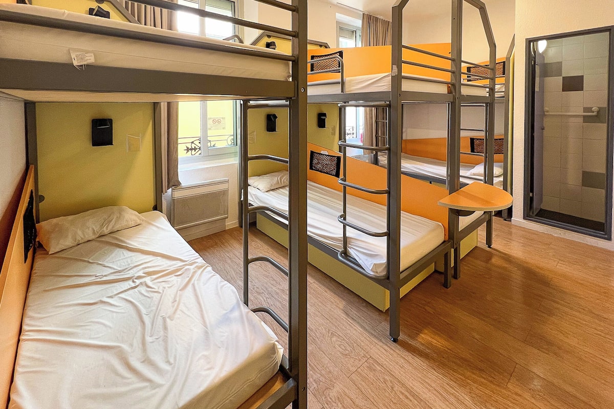 A dormitory room with bunk beds, a window, and a door.