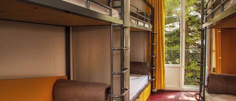 Habitación tipo dormitorio con literas, una ventana con cortinas amarillas y vistas a la vegetación.