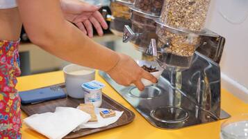 A person selecting granola from a dispenser, with a phone, yogurt cup, and napkin on a tray.